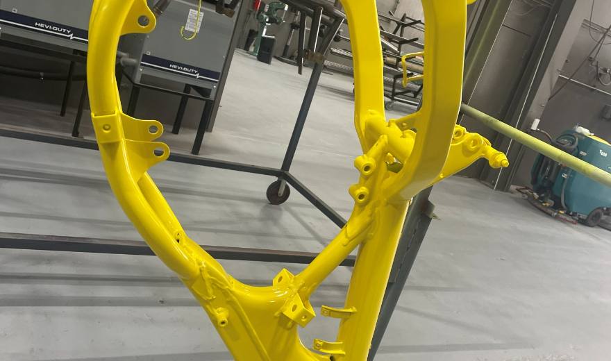 A motocross frame finished in bright yellow powder coat, standing on the shop floor