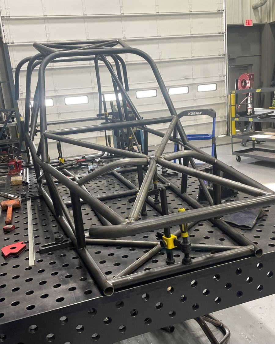 An off-road cage tacked up on the fixture table with the welder alongside
